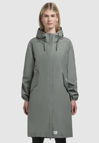 Jachetă impermeabilă de culoare verde măsliniu deschis, cu glugă, manșete elastice, două buzunare laterale și fermoar frontal. Material neted, cu textură.