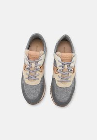 Une paire de baskets décontractées grises et beiges avec des lacets à motifs, des accents en cuir et un doublure douce, présentées de dessus sur un fond blanc.