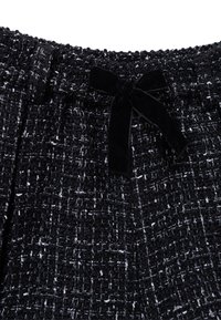 Tessuto testurizzato in bianco e nero con un motivo intrecciato, dotato di una vita elastica e un accento in velluto a forma di fiocco nella parte anteriore.