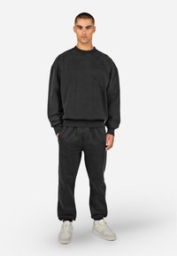 Black sweatshirt and matching joggers made from soft, textured material. Features ribbed cuffs and an elastic waistband; logo detail on chest.