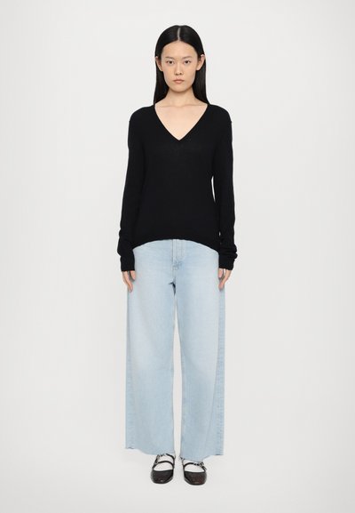 Zwarte V-hals trui, lange mouwen, gedragen met lichtblauwe wijde jeans en zwarte strap schoenen. Soepele textuur, casual stijl.
