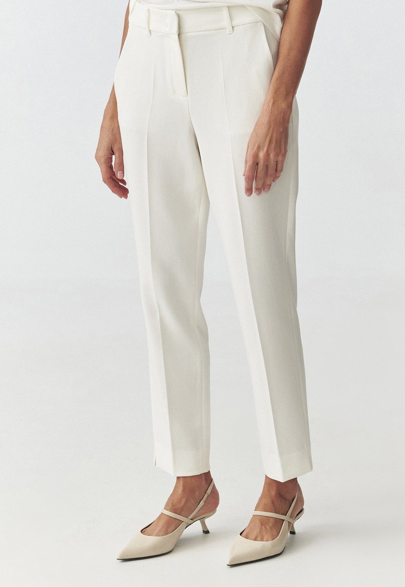 White tailored pants with a high waist, straight legs, and a smooth texture. Worn with light beige pointed-toe heels.