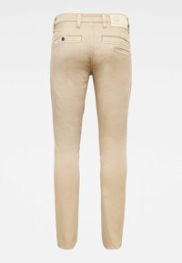 Pantalones de algodón beige con un corte slim, que cuentan con dos bolsillos traseros, un cierre de botón y una etiqueta con el logotipo en la cintura.