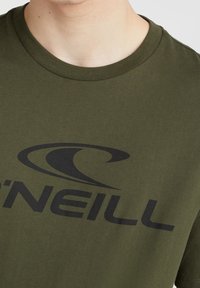 Camiseta de algodón verde con cuello redondo y un gran logo negro. El tejido parece suave, con una textura lisa y detalles de costura mínimos.