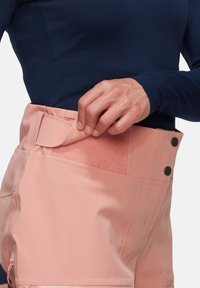 Pfirsichfarbene Shorts mit einer glatten Textur, ausgestattet mit einem Klettverschluss und zwei Knöpfen am Taillenbund, kombiniert mit einem marineblauen Oberteil.