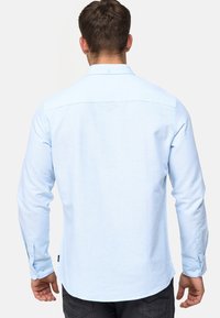 Himmelblaues Langarmhemd mit Button-Down-Kragen, strukturiertem Stoff und Knopfverschluss an den Handgelenken. Taillierte Passform mit abgerundetem Saum.