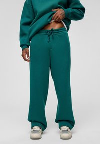 Teal oversized sweatshirt met een relaxte pasvorm, gecombineerd met bijpassende sweatpants met een koord in de taille en wijde pijpen, gedragen met sneakers.