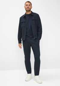 Marineblauwe ritssluitingjack met twee voorzakken, gecombineerd met een marineblauw T-shirt en bijpassende taps toelopende broek, afgewerkt met witte sneakers.