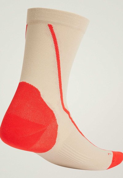 Calcetín beige con una superficie texturada, que presenta un toque de rojo brillante en el talón y en la punta. Raya roja vertical a lo largo del lado.