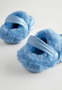 Helle blaue, flauschige Hausschuhe mit einer plüschigen Textur, ausgestattet mit verstellbaren Riemen und einer soliden Außensohle. Akzente sind aus weichem, flauschigem Material.