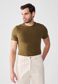 Olivengrønn t-skjorte med korte ermer laget av mykt materiale, tettsittende fasong, kombinert med lyse jeans, med en enkel rund hals.