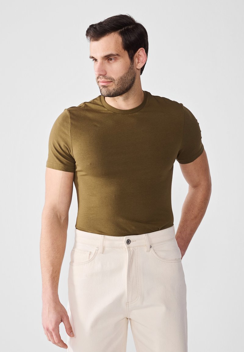 Olivengrønn t-skjorte med korte ermer laget av mykt materiale, tettsittende fasong, kombinert med lyse jeans, med en enkel rund hals.