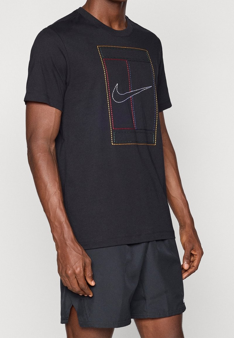 Homme portant un t-shirt noir Nike avec un motif rectangulaire multicolore cousu et un logo blanc Nike, associé à un short noir.