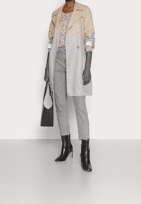 Beige- und grauer Farbverlauf-Trenchcoat, geknöpft, mit einem strukturierten Pullover und grauen Jeans, kombiniert mit schwarzen Stiefeletten und einer geflochtenen Handtasche.