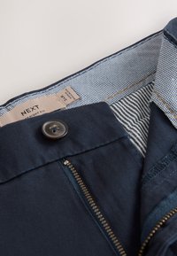 Marineblaue Hose mit Knopf und Reißverschluss, die gestreiftes und kariertes Innenfutter sowie ein Größenetikett mit 34R Straight Fit zeigt.