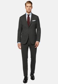 Costume gris ajusté avec une veste à deux boutons, revers crantés et poches avant ; associé à une chemise bleu clair et une cravate rouge foncé. Chaussures noires.
