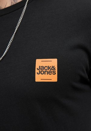 Black shirt with orange square logo reading "Jack & Jones" on chest, worn with a silver chain necklace.