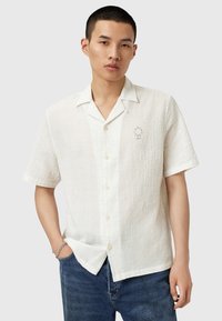 Chemise à manches courtes, tissu blanc texturé, boutonnière à l'avant, col à cran, petit logo brodé sur la poitrine gauche, assortie à un jean en denim bleu.