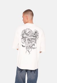 Hvid oversized t-shirt med et detaljeret sort grafik af en ørner med skriftruller på ryggen. Behagelig pasform med korte ærmer.