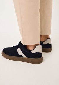 Marina skor i mocka med beige detaljer, med en texturerad yta, rund tå och en brun gummisula; snördesign framtill.