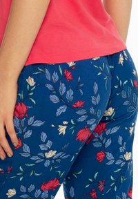 Floral print pants in blue fabric featuring red and white flowers with green leaves. The waistband is elastic, and the texture is smooth.
