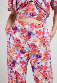 Ensemble à motif floral composé d'un haut à manches courtes et de pantalons à jambes larges. Le tissu présente des couleurs vives telles que le rose, l'orange et le violet, avec une texture douce.