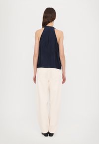 Navy satin halterneck top with a back zipper, paired with loose-fitting cream trousers featuring side pockets and flat black shoes.