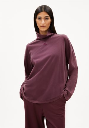 Übergroßer lila Pullover mit hohem Kragen und langen Ärmeln. Das weiche Baumwollmaterial bietet ein kleines gesticktes Logo auf der Vorderseite.