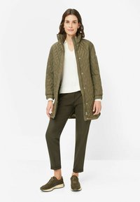 Quilted olivgrüne Jacke mit Stehkragen, Reißverschluss und Seitentaschen, kombiniert mit passenden Hosen und dunklen Sneakers.