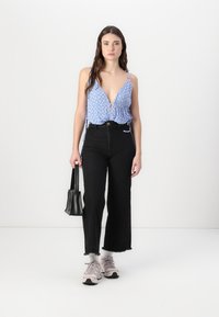 Blouse bleue à motifs avec un décolleté en V profond, associée à un jean noir à taille haute et à jambes larges. Complétée par un sac à main noir et des baskets légères.