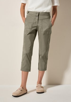 Olijfgroene cropped pants van lichte stof, met een knoopsluiting in de taille en meerdere zakken. Gecombineerd met beige instap schoenen.