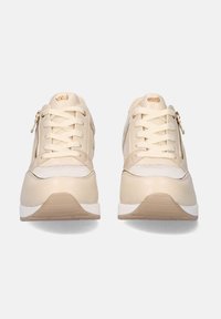 Zapatillas beige con un upper sintético liso, que presenta paneles de malla, cordones, cremalleras laterales y una suela de goma blanca. Los detalles incluyen herrajes en tono dorado.