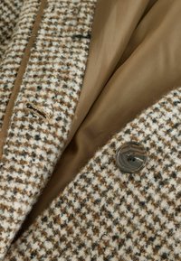 Cappotto in tweed beige e marrone con pattern a scacchi, foderato in morbido marrone, caratterizzato da un solo bottone e una piccola tasca con fessura.