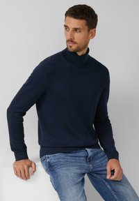 Marineblauer Rollkragenpullover aus weichem, gestricktem Material, mit langen Ärmeln und gerippten Bündchen. Kombiniert mit hellblauen Jeans.