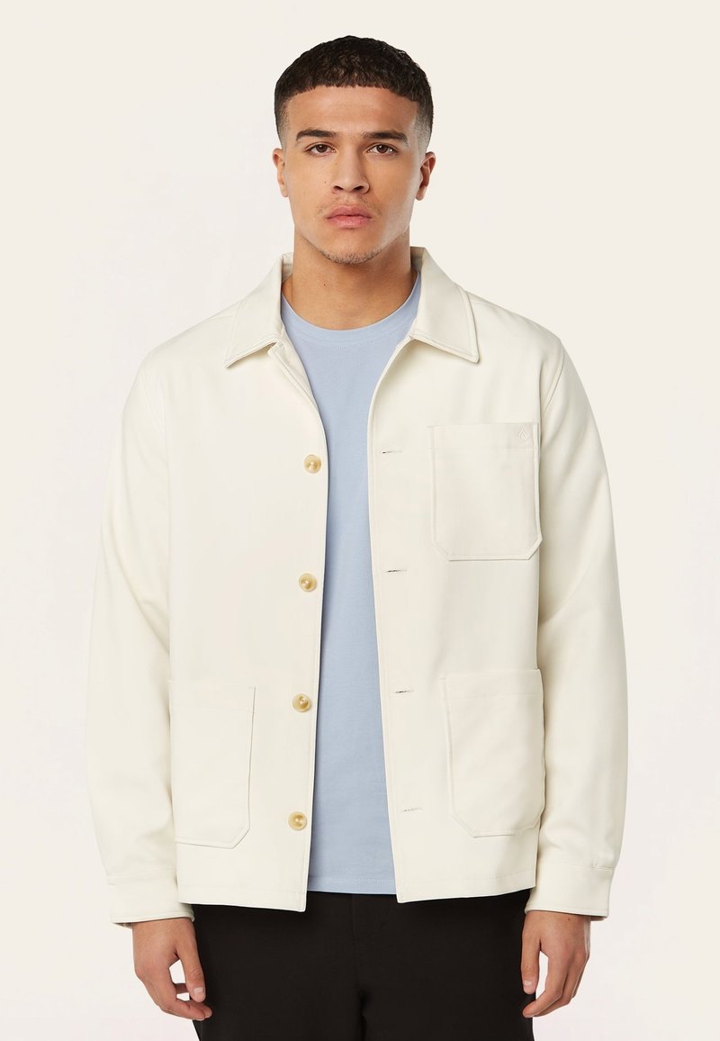 Witte button-up jas met twee voorzakken, lichtblauw binnenhemd. Zachte textuur, ontwerp met kraag en zichtbare stikseldetails.