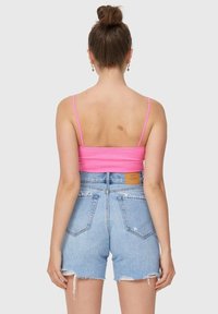 Rosa ribbad kort topp med tunna axelband, tillsammans med hög midja ljusblå jeansshorts med slitna nederkanter och en läderetikett på baksidan.