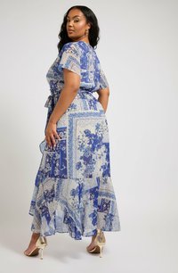 Maxi-mekko kevyestä kankaasta, jossa on sinisiä kukka- ja paisley-kuvioita. Mekossa on nauhavyötärö, lyhyet hihat ja kerroksellinen helma. Kultaiset korot täydentävät asun.