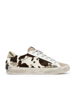 Sneaker low-top con stampa mucca marrone e bianca, punta beige, dettaglio glitter sul lato, lacci bianchi e suola bianca consumata.