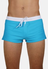 Shorts de bain bleus en tissu extensible avec une ceinture élastique blanche et un cordon de serrage. Possède une texture lisse et une coupe ajustée.