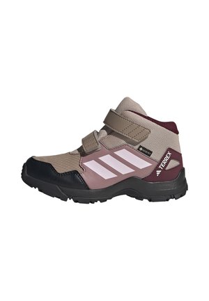 Zapato de senderismo para niño de altura media con malla beige, refuerzos sintéticos en rosa oscuro, suela negra, tiras de velcro y rayas blancas de Adidas a los lados.