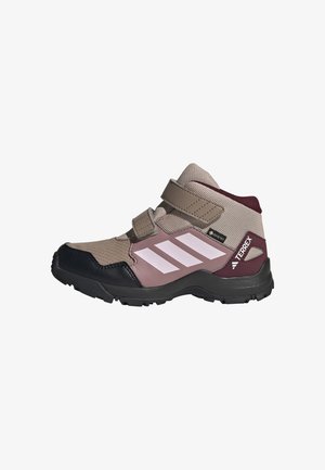 Chaussure de randonnée enfant de hauteur moyenne avec mesh beige, renforts synthétiques rose foncé, semelle noire, sangles velcro et bandes blanches Adidas sur le côté.