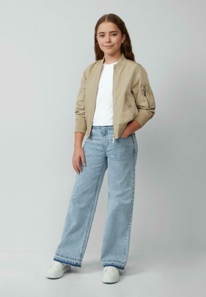 Beige Bomberjacke mit gerippten Bündchen, weißem T-Shirt, hellblauen weiten Jeans und weißen Sneakers. Glatte Textur und lässiges Design.