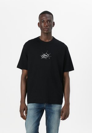 T-shirt en coton noir avec un logo graphique blanc au design éclaboussé au centre. Coupe ample et manches courtes.