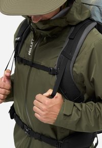 Veste imperméable vert olive avec une capuche ajustée, des sangles réglables et une couche extérieure texturée. Les caractéristiques comprennent une boucle et un cordon élastique.