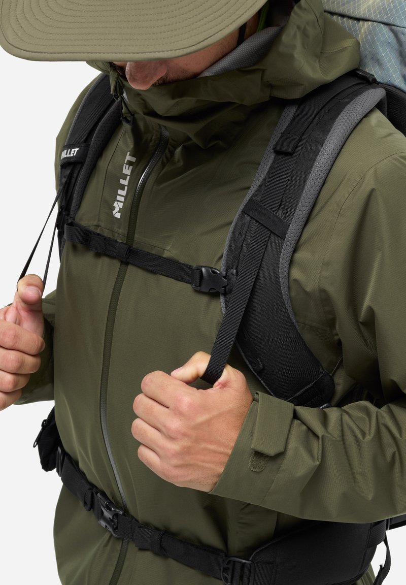 Veste imperméable vert olive avec une capuche ajustée, des sangles réglables et une couche extérieure texturée. Les caractéristiques comprennent une boucle et un cordon élastique.