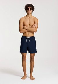 Shorts de bain pour hommes de couleur marine en tissu léger, avec une taille élastique ajustable par un cordon et un petit logo.