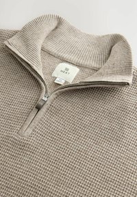 Beiger Strickpullover mit Reißverschluss, geripptem Kragen und strukturiertem Körper. Das Etikett zeigt "NEXT" mit der Größe "M".