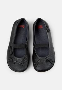Bailarinas de cuero negro con acabado texturizado, punta redondeada, bandas elásticas y lazos en la parte delantera. Forro interior suave.