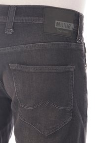 Los vaqueros de mezclilla negra presentan una superficie texturizada, costuras en contraste y un parche de cuero con "MUSTANG True Denim" en la cintura.