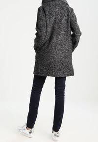 Grå uldfrakke med tekstureret finish, hætte og to sidelommer, kombineret med mørke slim-fit bukser og sølv sneakers.